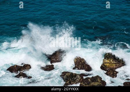 Raue Meereswellen, die an der Küste oder am Strand auf Felsen krachen Stockfoto
