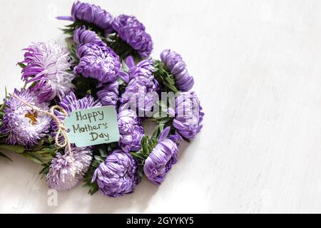 Festlicher Hintergrund mit einem Strauß blauer Chrysanthemen und einer Grußkarte mit dem Wunsch nach einem glücklichen Muttertag auf weißem Hintergrund, Kopierfläche. Stockfoto