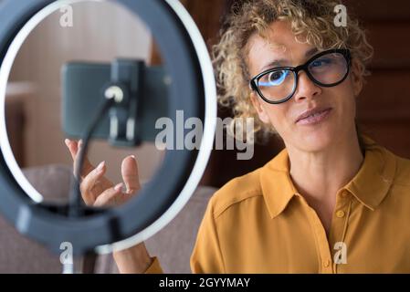 Junge Bloggerin, die Videos auf dem Smartphone und mit Ringlampe im Wohnzimmer zu Hause aufzeichnet. Weibliche Vloggerin, die neue Videos für das Teilen auf Social Me macht Stockfoto