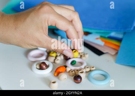 Nahaufnahme der Hände einer unbekannten Designerin, die am Tisch arbeitet - Hand einer Frau, die handgefertigte Holz-Plastikringe und Perlen hält, um Material zu wählen Stockfoto