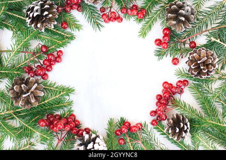 Weihnachten und Neujahr Hintergrund, grüne Tannenzweige und rote Beeren sind auf einem hellen Hintergrund gerahmt Stockfoto