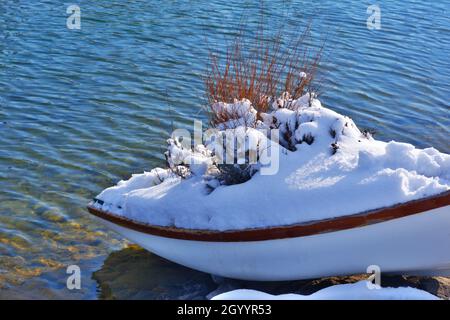 Kleines Ruderboot aus Holz am See im Winter unter Schnee Stockfoto