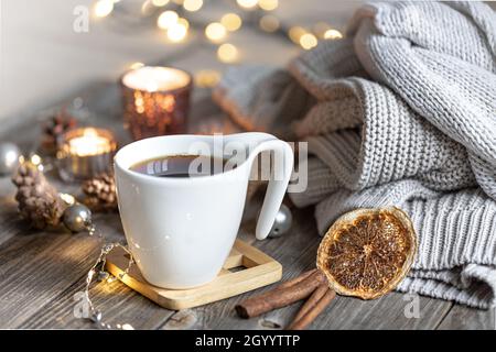 Gemütliches Zuhause Winter Komposition mit einer Tasse Tee auf einem verschwommenen Hintergrund mit brennenden Kerzen und Bokeh Lichter und gestrickte Elemente. Stockfoto