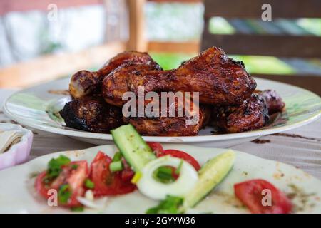 Hühnerschenkel unter Grillsauce und Kartoffelscheiben, die auf einem Holzkohlegrill gebacken und geräuchert wurden Stockfoto