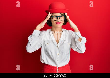 Junge Brünette Frau trägt Stewardess Stil und Brille leiden unter Kopfschmerzen verzweifelt und gestresst, weil Schmerzen und Migräne. Hände auf dem Kopf. Stockfoto