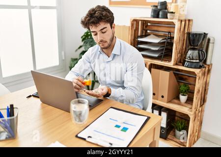 Junger hispanischer Geschäftsmann mit ernstem Ausdruck nimmt Pillen im Büro. Stockfoto