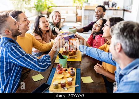 Lächelnde, multirassische Gruppe junger Menschen, die zusammen frühstücken und lachen Stockfoto