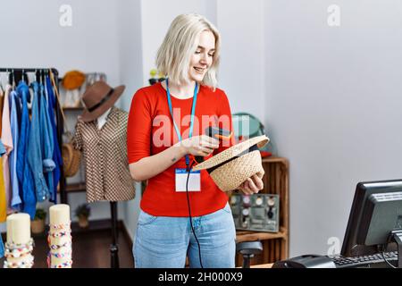 Junge kaukasische Frau lächelt selbstbewusst mit Barcode-Lesegerät im Bekleidungsgeschäft Stockfoto