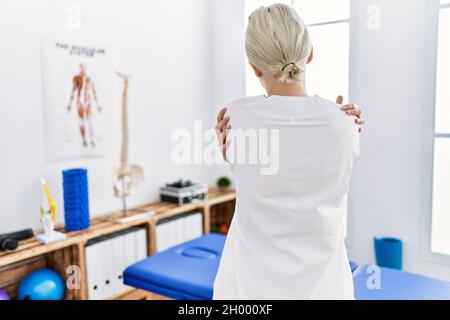 Junge kaukasische Frau, die in der Schmerzheilungsklinik arbeitet, umarmte sich glücklich und positiv von hinten. Selbstliebe und Selbstversorgung Stockfoto