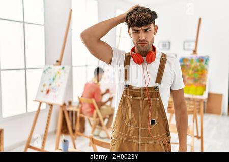 Junger hispanischer Mann im Kunststudio verwirrt und wundert sich über Fragen. Unsicher mit Zweifel, Denken mit Hand auf Kopf. Nachdenkliches Konzept. Stockfoto