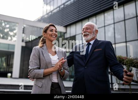 Reifer Geschäftsmann und junge Frau reden und lachen vor dem Bürogebäude Stockfoto