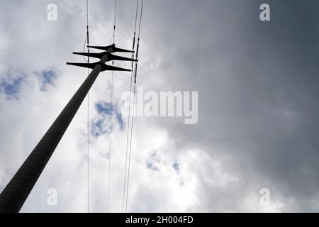 Betonmast für Hochspannungs-Stromtransport und -Versorgung. Low-Angle-Ansicht mit dramatischem Himmel im Hintergrund. Kopierplatz verfügbar. Stockfoto