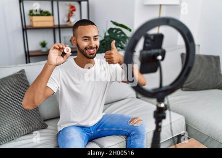afroamerikanischer Mann, der Vlog Tutorial über Bitcoin mit Smartphone zu Hause aufzeichnet, lächelt glücklich und positiv, Daumen hoch, tut ausgezeichnet und Zustimmung s Stockfoto