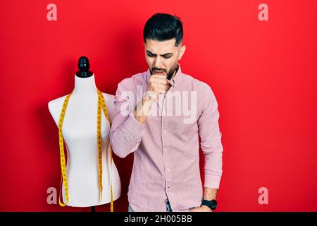 Schöner Schneidermann mit Bart, der an der Übungspuppe steht, sich unwohl fühlt und Husten als Symptom für Erkältung oder Bronchitis. Gesundheitskonzept. Stockfoto