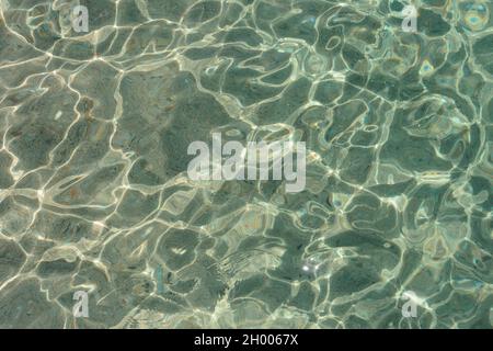 Muster der Sonnenflecken ist in klarem Meerwasser unter Kieselstein auf dem Meeresboden. Stockfoto