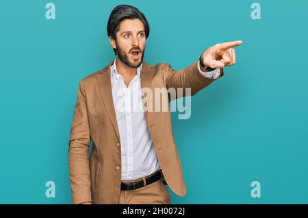 Junger hispanischer Mann in Geschäftskleidung mit dem Finger überrascht vor, offener Mund erstaunt Ausdruck, etwas auf der Vorderseite Stockfoto
