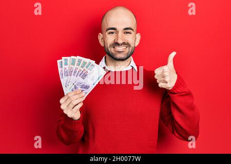 Junger kahler Mann mit ägyptischen Pfund-Banknoten, der glücklich und positiv lächelt, tut vortrefflich und genehmigt das Zeichen Stockfoto