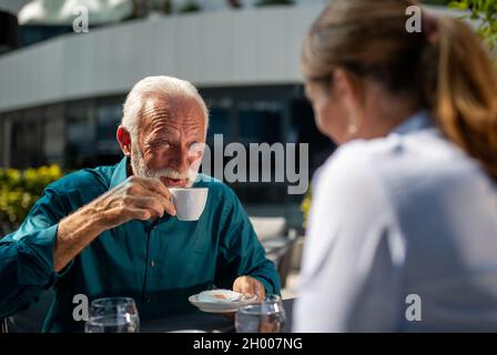 Reifer erwachsener Geschäftsmann, der Kaffee im Café im Freien trinkt und in eine hübsche junge Frau schaut Stockfoto