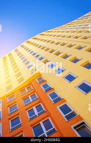 Modernes, mehrstöckiges europäisches Gebäude mit vielen Glasfenstern, die vor dem Hintergrund des blauen Himmels und der Sonne stehen. Wohngebäude, urban real Stockfoto