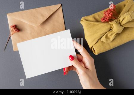 Frau mit Mockup-Karte über dem grauen Tisch mit furoshiki-Geschenk Stockfoto