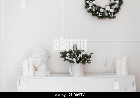 Weihnachtliches Bouquet aus Fichte und Baumwolle in einem weißen Interieur vor dem Hintergrund eines weißen Klaviers Stockfoto