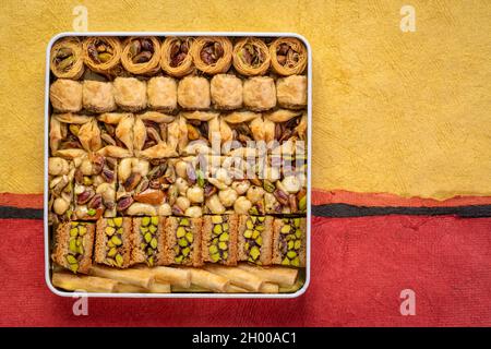 Auswahl an traditionellem türkischen Baklavagebäck in einer Blechdose, ein Dessert ist auch als persischer oder libanesischer Baklava bekannt, texturierter Papierhintergrund Stockfoto