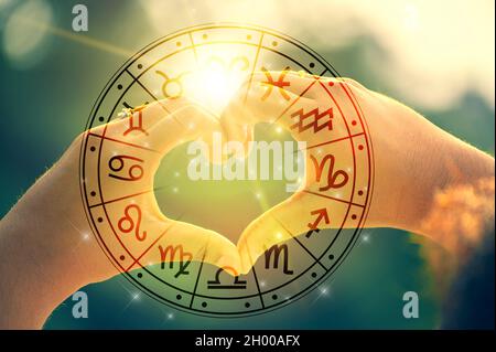 Die Hände von Frauen und Männern sind die Herzform, wobei das Sonnenlicht, das durch die Hände geht, astrologische Symbole hat Stockfoto