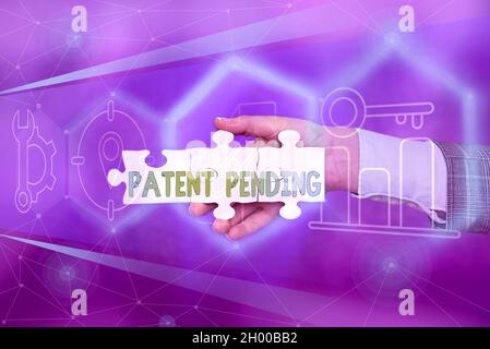 Schild mit der Anzeige „Patent angemeldet“. Wort geschrieben auf Anfrage bereits eingereicht, aber noch nicht gewährt Verfolgung Schutz Hand Holding Jigsaw Puzzle Stück Stockfoto