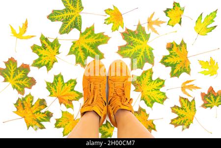 Weibliche Füße in leuchtend orangefarbenen Sneakern, die auf pigmentierten Blättern auf weißem Hintergrund stehen. Herbst Saison Mode Hintergrund. Stockfoto