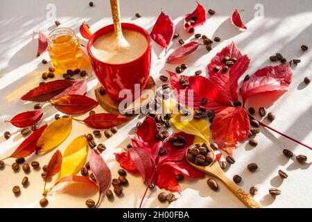 Tasse heißen Kaffee inmitten gerösteter Kaffeebohnen und roter und gelber Herbstblätter auf einem Tisch Stockfoto