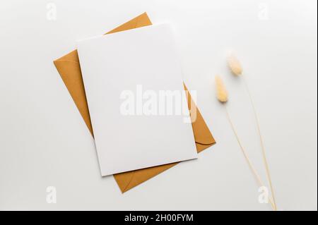 Grußwort, Hochzeit oder Glückwünsche Briefpapier Mockup. Unbeschriftete Grußkarte auf Bastelumschlag und zwei Grashalme mit Hasenschwanz. Stockfoto