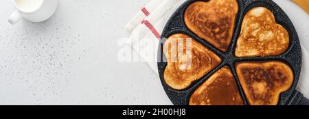 Pfannkuchen in Form von Frühstücksherzen mit Schokoladensauce in grauer Keramikplatte, Tasse Kaffee auf grauem Betongrund. Tabelleneinstellung für Valenti Stockfoto