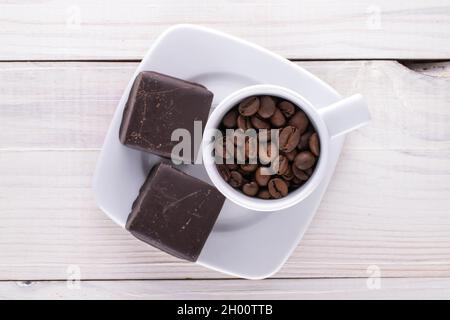 Zwei süße Pralinen mit einer Untertasse und einer Tasse mit Kaffeekörnern auf einem Holztisch, Nahaufnahme, Draufsicht. Stockfoto