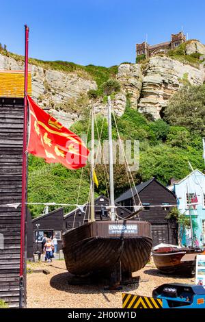 Die Flagge von East Sussex fliegt mit Fischerbooten an der Küste von Hastings in East Sussex, England, mit der Standseilbahn in der Ferne Stockfoto