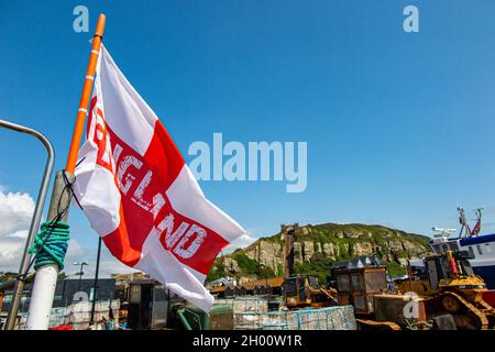 Die Flagge von St. George wird von Fischerbooten an der Küste von Hastings in East Sussex, England, mit der Standseilbahn in der Ferne überflogen Stockfoto