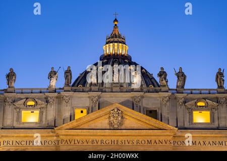 Kuppel, Statuen von Jesus und Aposteln und Wappen im Giebel des Petersdoms in der Vatikanstadt bei Einbruch der Dunkelheit. Stockfoto