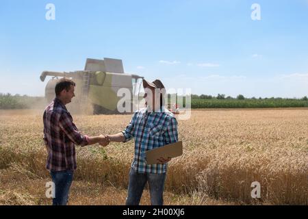 Zwei Bauern schüttelten sich während der Ernte im Weizenfeld die Hände, im Hintergrund der Mähdrescher Stockfoto
