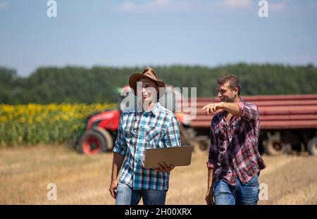 Zwei Bauern, die während der Ernte im Weizenfeld spazieren. Traktor mit Anhänger für Getreide im Hintergrund