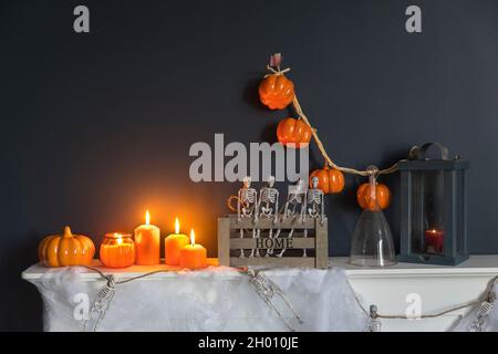 Halloween-Heimtextilien. Plastikspielzeug-Skelette in einer Holzkiste am Kamin vor einer dunkelblauen Wand. Eine Girlande aus Skeletten. Spinnennetz auf der Kommode. Stockfoto