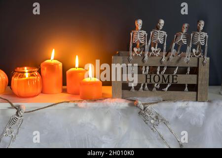 Halloween-Heimtextilien. Plastikspielzeug-Skelette in einer Holzkiste am Kamin vor einer dunkelblauen Wand. Eine Girlande aus Skeletten. Spinnennetz auf der Kommode. Stockfoto