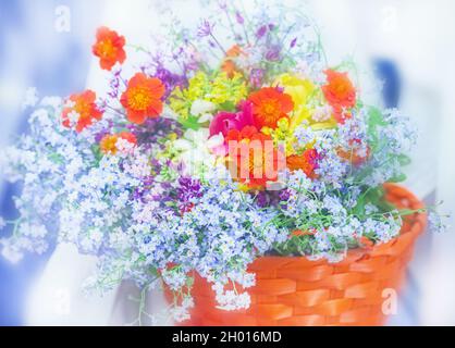 Charmanter mehrfarbiger Strauß von fröhlichen Sommerblumen in orangefarbenem Korb Stockfoto