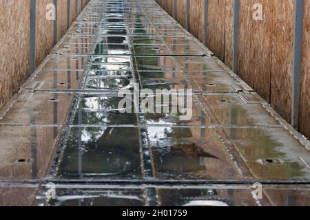 Die Straße ist im Frühjahr mit Pfützen bedeckt. Metallbrücke über den Fluss nach Regen. Pfützen auf der Straße. Reflexion nach Regen, Landschaftsansicht Stockfoto