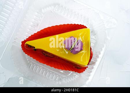 Gelbes Stück Kuchen mit Macarons und Gelee von oben. Käsekuchen mit Mango auf Mürbeteig. Köstliches, helles Dessert auf einem weißen Teller. Zitrone so Stockfoto