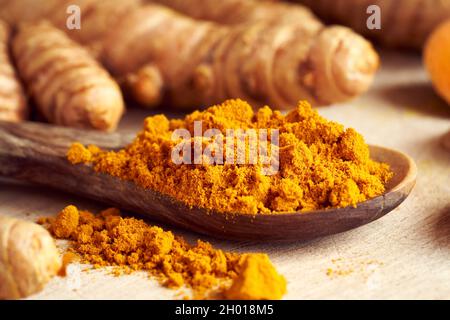 Gemahlenes Curcuma-Pulver auf einem Löffel, mit frischer Kurkuma-Wurzel im Hintergrund Stockfoto