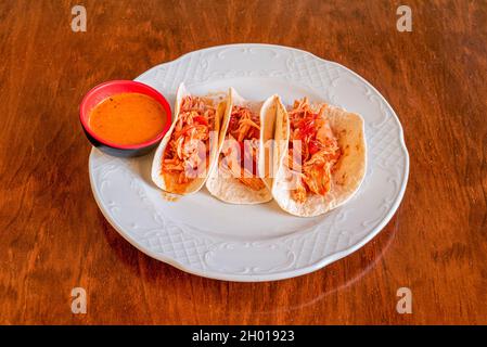Mexikanisches Hähnchen Tinga Tacos mit Pull-Hähnchenfleisch-Eintopf, Dipping-Sauce und Weizentortillas Stockfoto