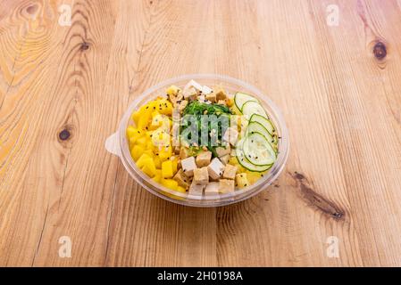 Vegane Schüssel mit gebratenen Tofu-Würfeln, Ananas- und Mangowürfeln, Mandel-Torozos, Gurkenscheiben mit Wakame-Algensalat und Mohn Stockfoto