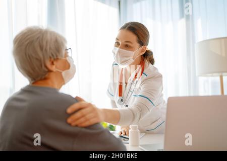 Arzt und ältere Frau mit Gesichtsmasken während des Coronavirus- und Grippeausbruchs. Virenschutz. COVID-2019. Masken übernehmen. Stockfoto