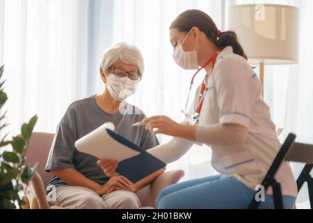 Arzt und ältere Frau mit Gesichtsmasken während des Coronavirus- und Grippeausbruchs. Virenschutz. COVID-2019. Masken übernehmen. Stockfoto