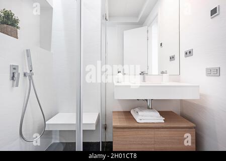 Badezimmer mit gefliester Dusche in weißen Farbtönen mit Holzschrank und weißem Waschbecken in der Ferienwohnung Stockfoto