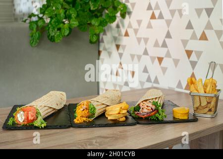 Sortiment von Wraps gefüllt mit gebratenem Huhn mit Gemüse und Senfsauce, gebratenen Fisch mit Cheddar-Käse und Pommes frites, s Stockfoto